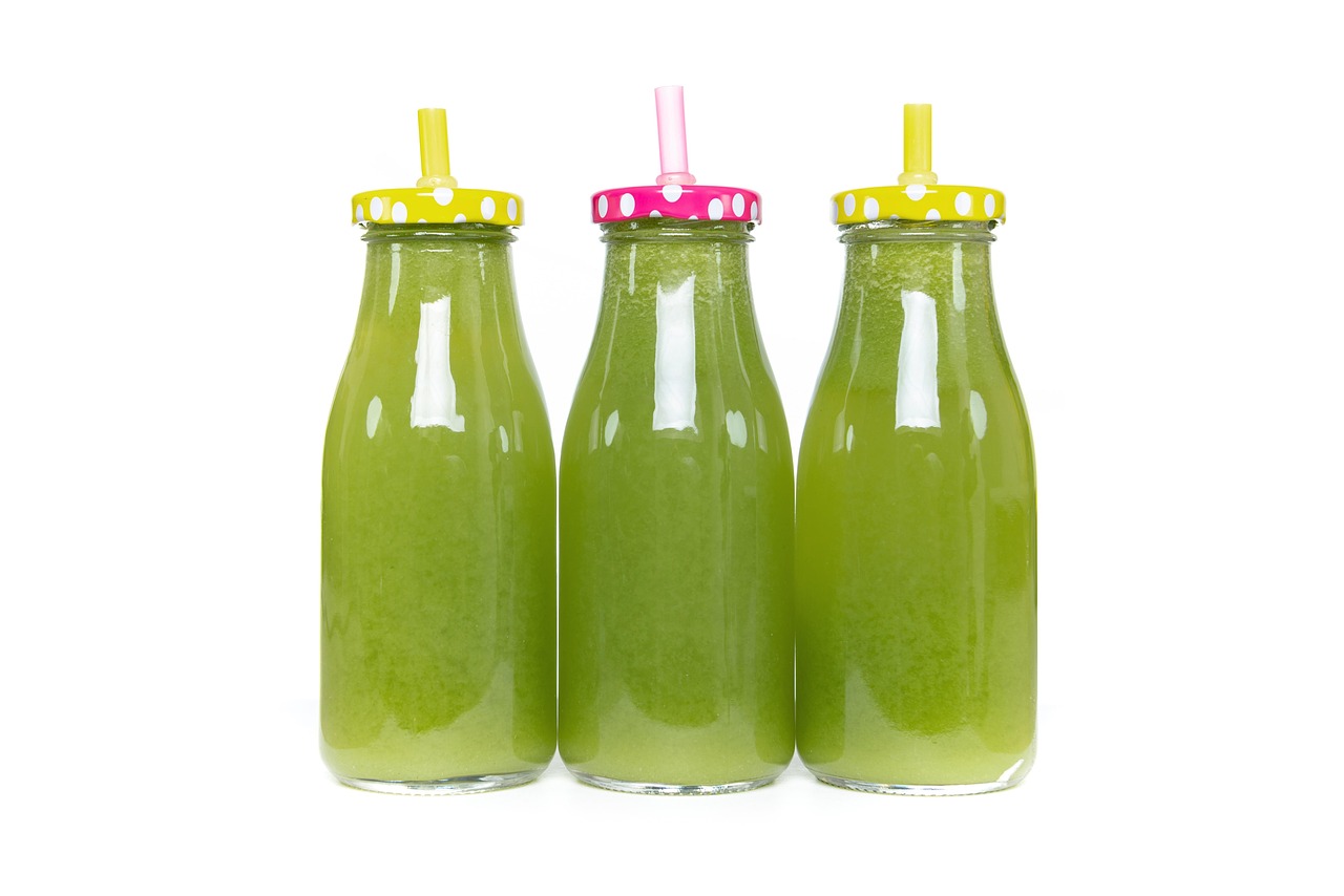 Three small bottles of pale green celery juice on a white background