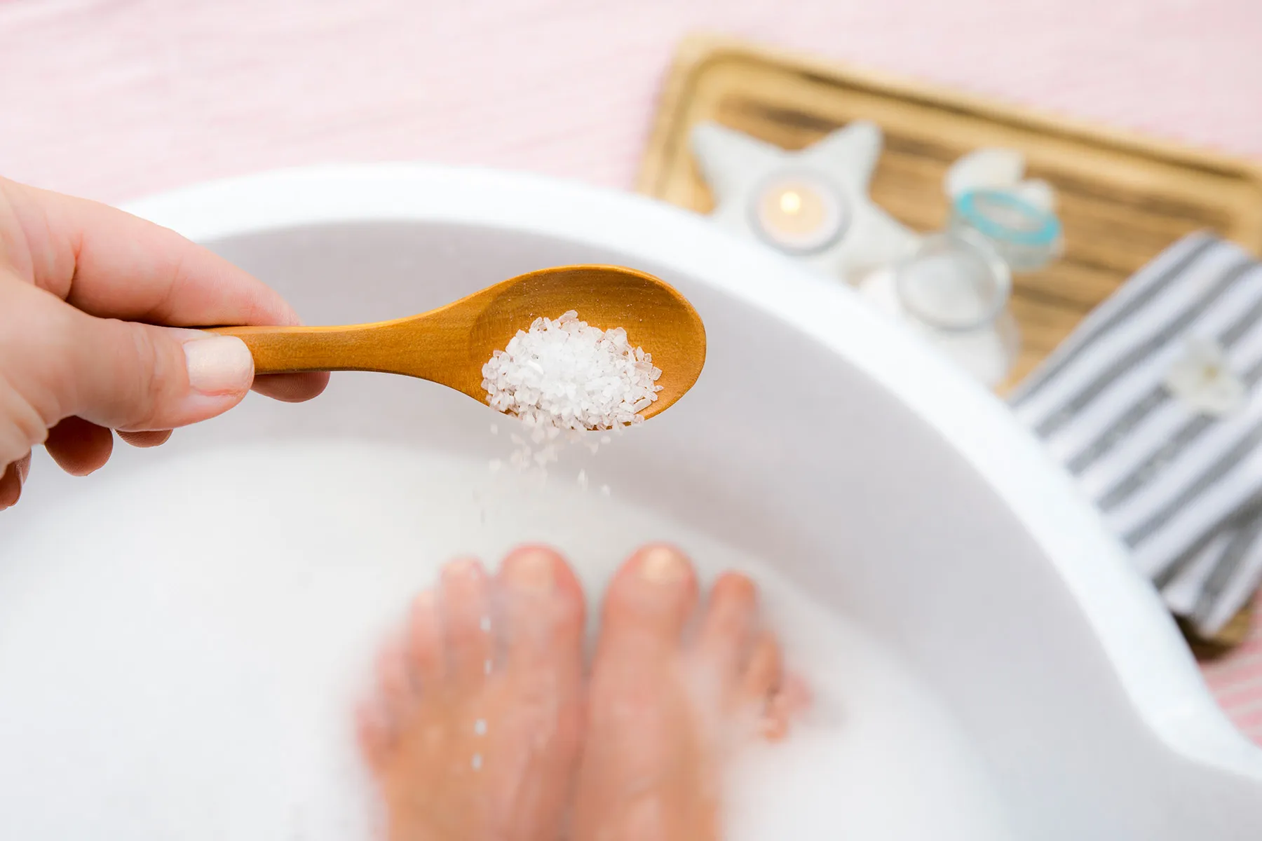 Wooden spoon holding bath salts over a warm foot soak