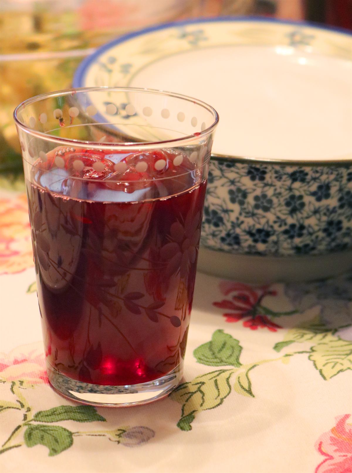 Glass of deep red hibiscus tea on a floral tablecloth