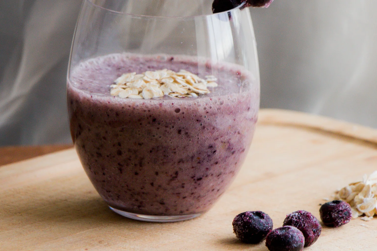 Purple blueberry oat smoothie topped with rolled oats beside frozen blueberries
