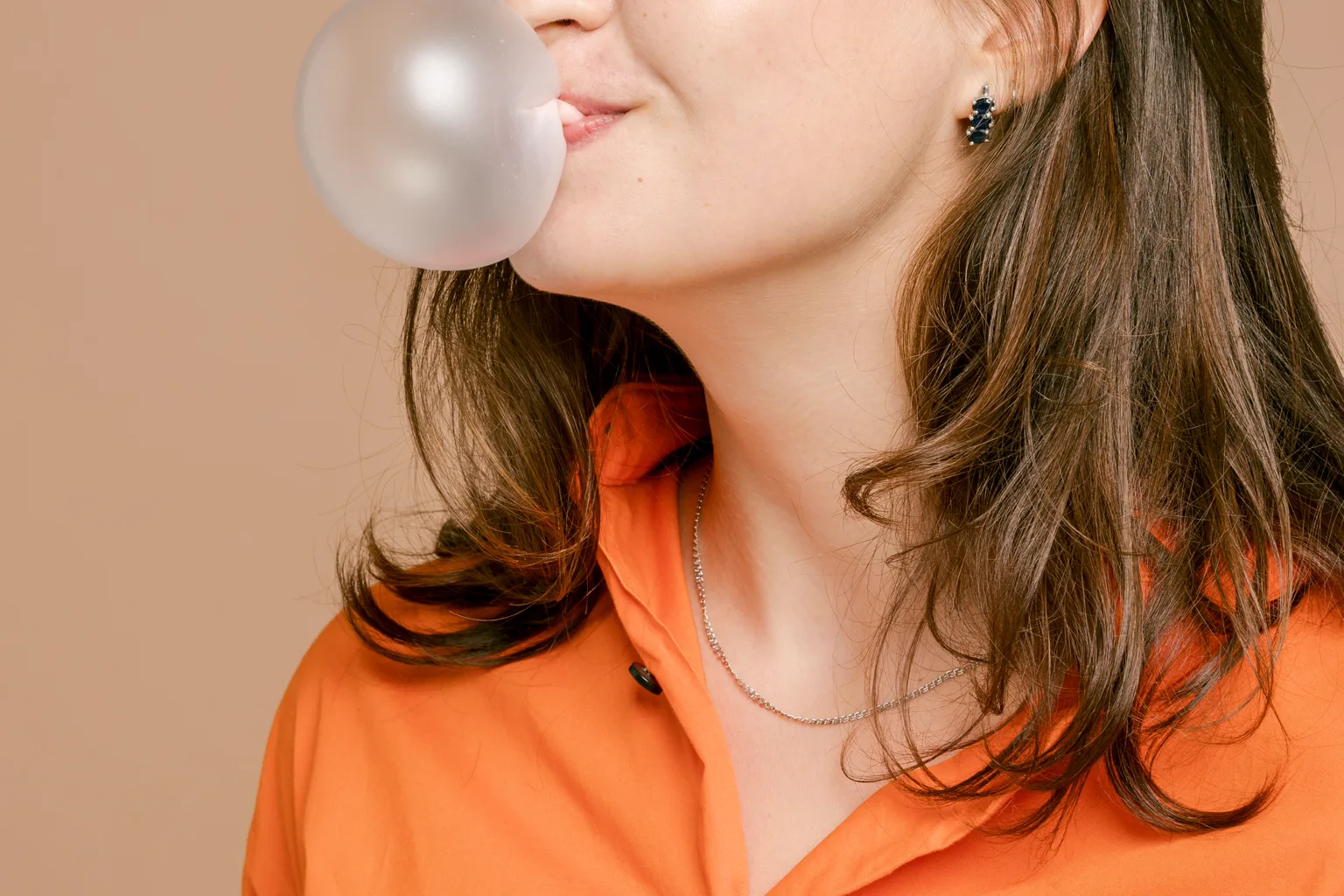 Side view of a woman blowing a bubble with chewing gum, showing the jaw and chin area