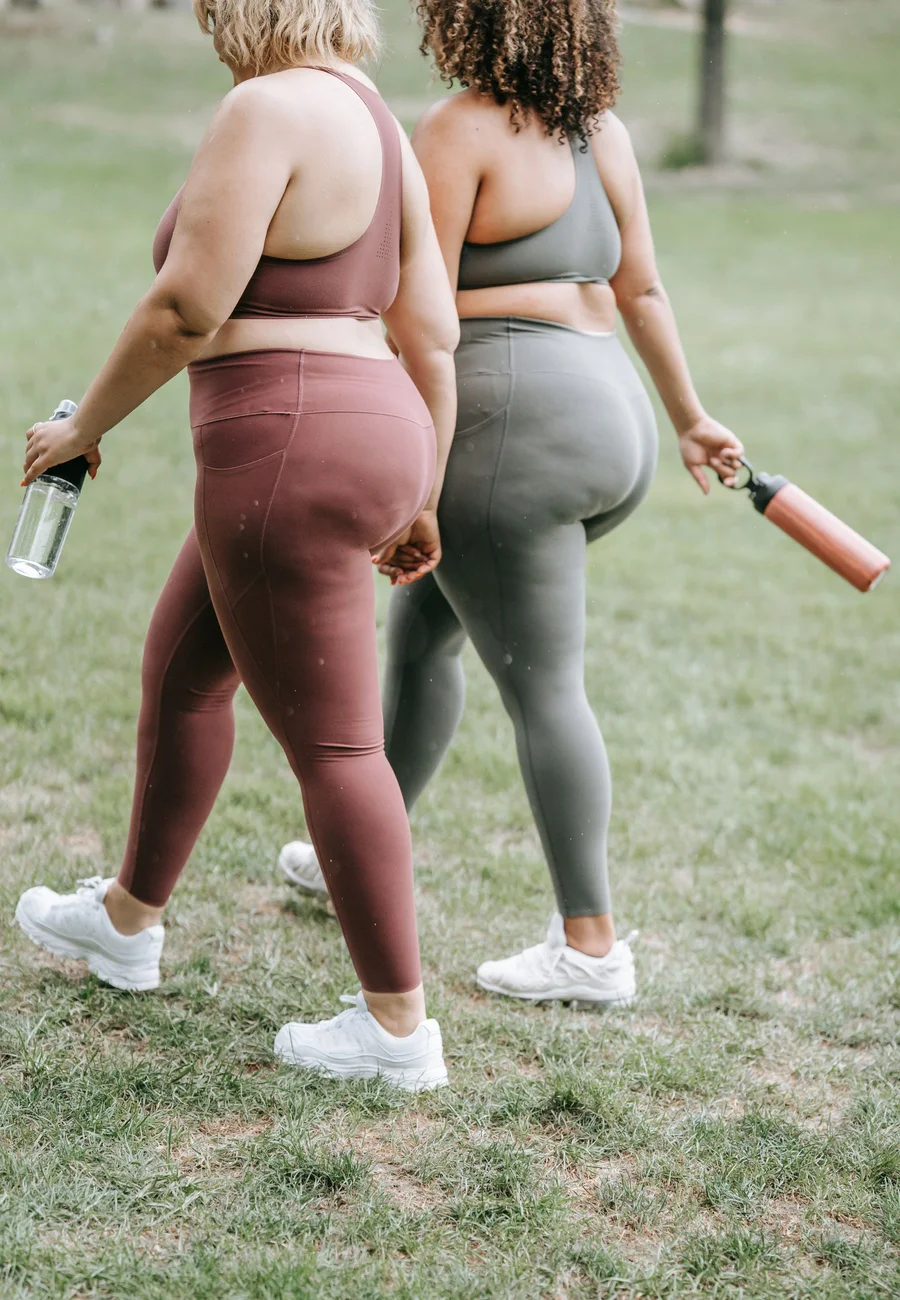 Two women in sports clothing walking outdoors with water bottles