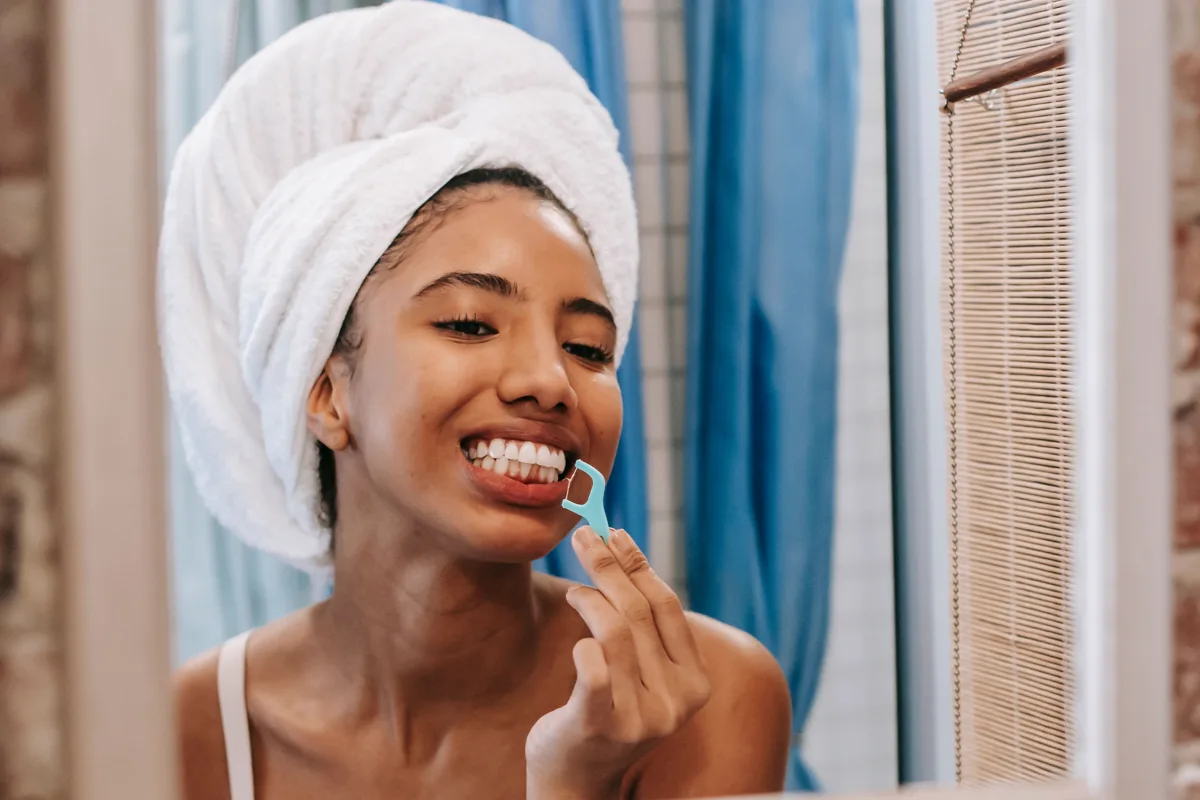 Woman carefully flossing her teeth in front of a bathroom mirror