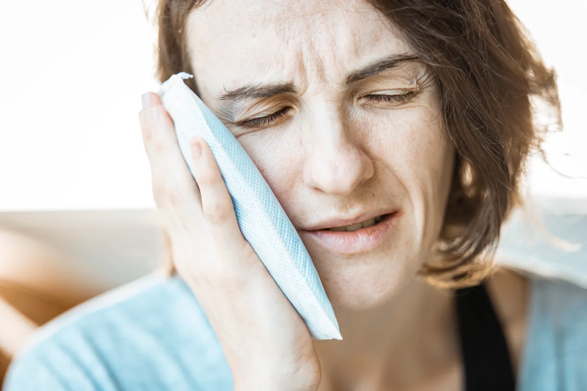 Woman holding a cold compress against her cheek for dental discomfort