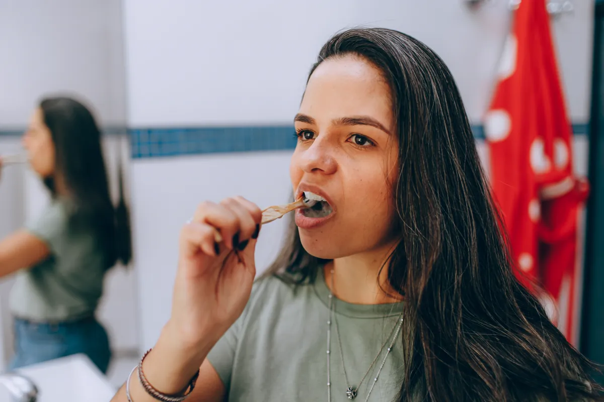 Woman gently brushing her teeth while looking in a bathroom mirror