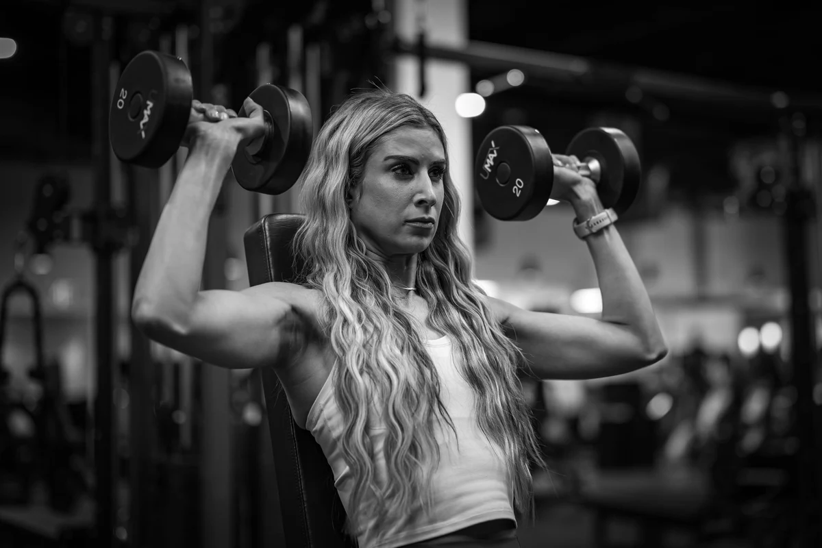 Woman performing a seated dumbbell strength exercise in a gym