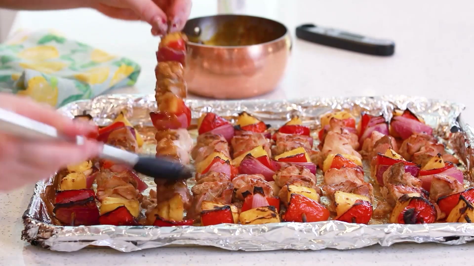 Glazed chicken kebabs being brushed on a foil-lined baking tray